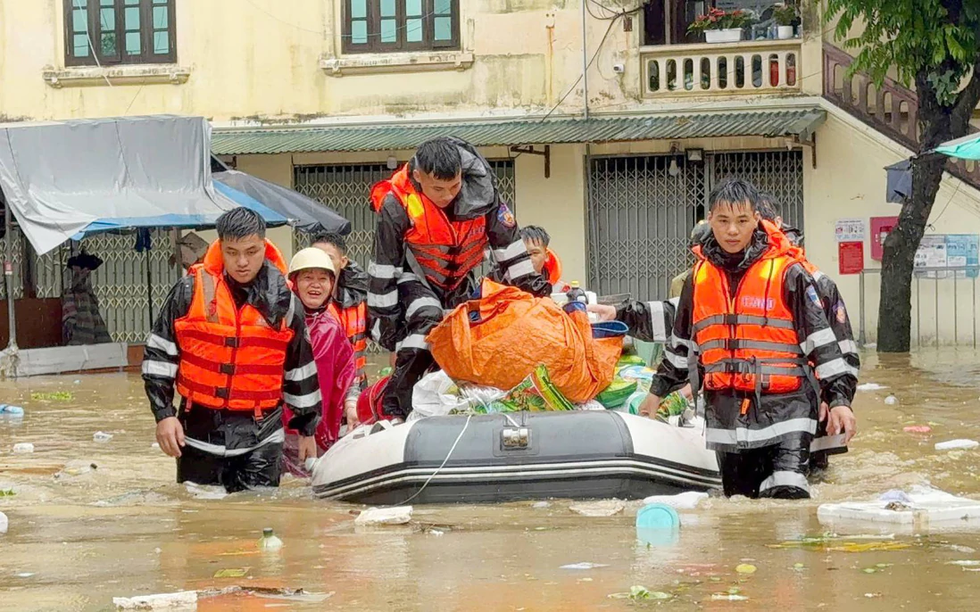Rescue workers in life jackets guiding a boat of residents and supplies through a flooded street in Lạng Sơn