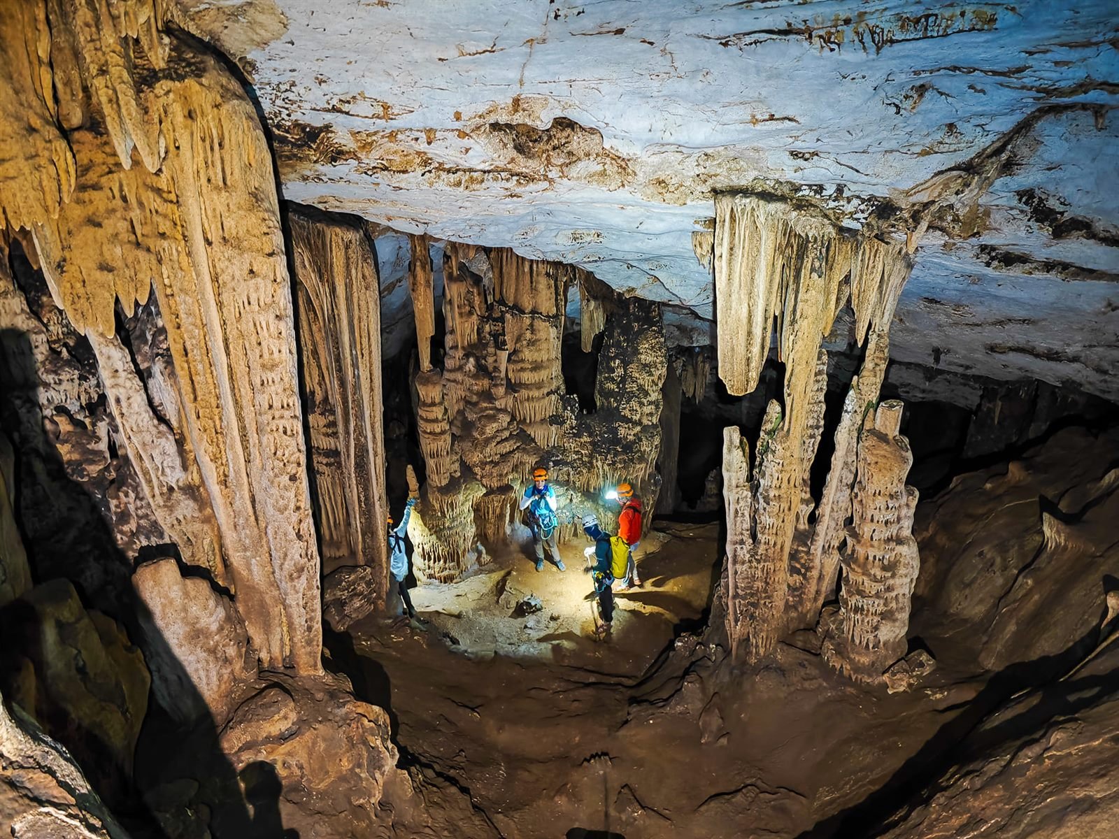 Cavers with headlamps standing among tall stalactites and stalagmites